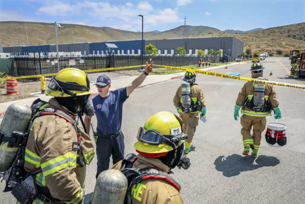 Firemen enter the burning area around the energy storage facility dressed in full gear with rebreathers on their back.